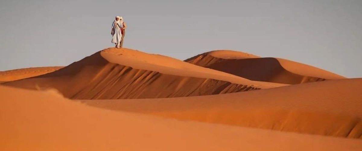 2 personnes dont 1 nomade an haut d'une dune dans le désert
